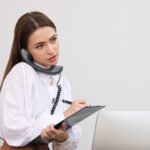Front desk worker taking a phone call while writing in a medical spa