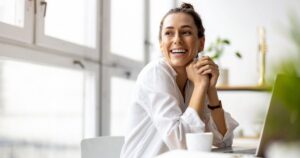 Smiling woman sitting at a laptop in a bright modern office.